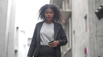 A black woman is getting ready for work in an office uniform in a public downtown area, carrying all her work equipment including a computer and a phone. video