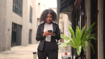 A black woman is getting ready for work in an office uniform in a public downtown area, carrying all her work equipment including a computer and a phone. video