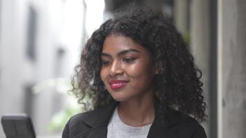 A black woman is getting ready for work in an office uniform in a public downtown area, carrying all her work equipment including a computer and a phone. video