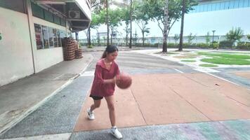 A woman plays basketball alone in a public area, having fun and practicing at the same time. video