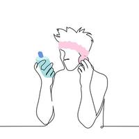 man applies a cosmetic product to his face with a sponge while reading the text on the bottle of the product - one line art . concept of a modern man taking care of his facial skin vector