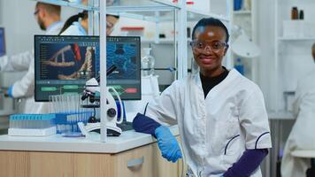 Professional black woman scientist looking at camera smiling in modern equipped lab. Multiethnic team examining virus evolution using high tech and tools for scientific research, vaccine development. photo