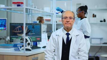Senior chemist sitting in modern equipped lab looking satisfied at camera. Multiethnic team examining virus evolution using high tech and chemistry tools for scientific research, vaccine development photo