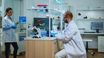 Scientist working in modern equipped laboratory cheching virus development with microscope. Multiethnic team examining vaccine evolution using high tech and chemistry tools for scientific research. photo