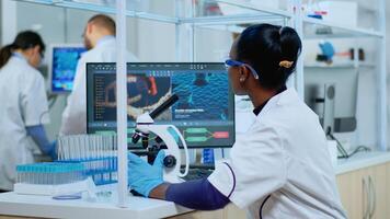 African woman scientist using microscope in modern equipped lab. Multiethnic team examining virus evolution using high tech for scientific research of treatment development against covid19. photo