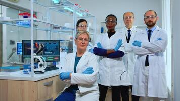 Multiethnic team of experienced scientists looking at camera in modern equipped lab. Group of doctors examining virus evolution with high tech and chemistry tools for scientific research, vaccine development of covid19 photo