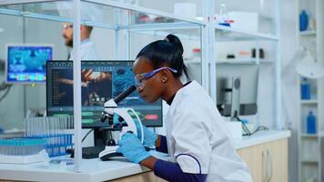 African scientist checking sample of virus using microscope in modern lab. Multiethnic team examining vaccine evolution using high tech for scientific research of treatment development against covid19 photo