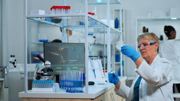 Microchemist doing research checking liquid in test tube typing results on pc in modern equipped lab. Multiethnic team examining virus evolution using high tech for vaccine development against covid19 photo