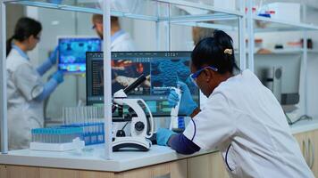 Black woman chemist analysing reaction of virus on microscope in laboratory. Multiethnic team examining vaccine evolution using high tech for scientific research, treatment development against covid19 photo