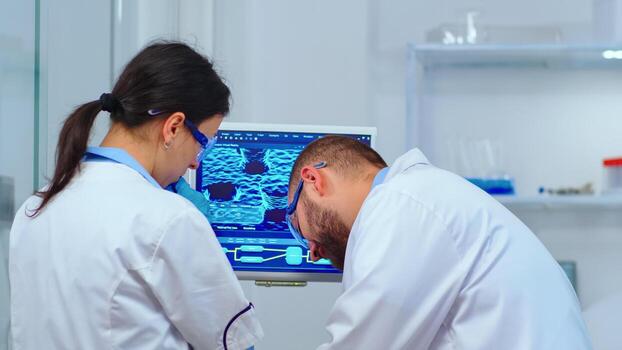 Team of scientists discussing about virus development in front of pc in modern equipped laboratory. Multiethnic stuff analysing vaccine evolution using high tech for researching treatment photo