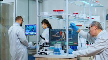 Elderly man technologist doing a laboratory test examining a flask with a blue substance, chemist holding tube with liquids inside. Scientist working with various bacteria tissue and blood samples photo