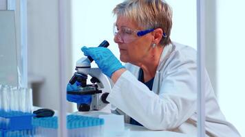 Senior scientist doing investigation using microscope in equipped laboratory. Multiethnic stuff examining vaccine evolution using high tech and technology researching diagnosis against epidemic virus photo