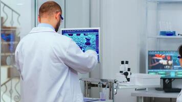 Professional chemist analysing vaccine development using touchscreen display in modern equipped laboratory. Man examining virus evolution using high tech researching diagnosis against covid19 photo
