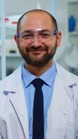 Portrait of scientist man smiling at camera sitting in modern equipped laboratory. Multiethnic team examining virus evolution using high tech and chemistry tools for scientific research, vaccine development. photo