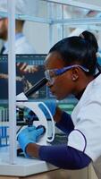 Black woman chemist analysing reaction of virus on microscope in laboratory. Multiethnic team examining vaccine evolution using high tech for scientific research, treatment development against covid19 photo