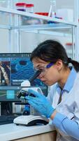 Scientist team checking virus development using microscope and writing analysis results on tablet in modern equipped lab. Multiethnic group examining vaccine evolution using high tech for research. photo