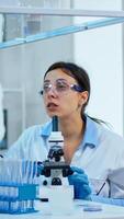Team medical scientist conducting DNA experiments under digital microscope writing results into tablet working in science laboratory. Caucasian lab engineer in white coat analysing vaccine development photo
