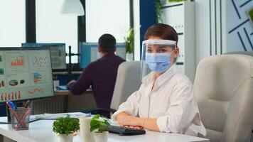 Manager woman with visor and protection mask looking at camera smiling in new normal business office. Business team working in financial company respecting social distance during global pandemic. photo