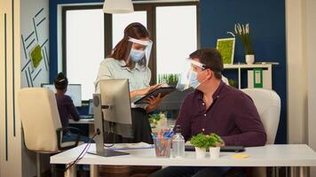 Workers talking about project typing on pc and tablet wearing protection face masks in office room during coronavirus. Multiethnic team working in company with new normal respecting social distance. photo