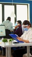 Teamworkers in new normal office making financial strategy wearing protective mask. Employees with visors working in corporate company workspace respecting social distance analysing data and graphs. photo