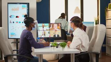 Black woman and comapany entrepreneur wearing protective masks talking with remotely colleagues on call. New normal business office Multiethnic team working respecting social distance. photo