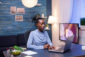 Dark skinned business woman using laptop track pad working overtime to finish a deadline. Black entrepreneur sitting in personal workplace writing on keyboard. photo
