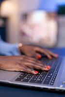 Side view of african woman hands typing on laptop working on deadline for company. Employee using modern technology network wireless doing overtime. photo