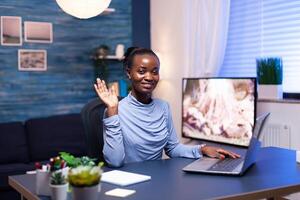 Dark skinned entrepreneur waving in the course of conversation during remote call. African business woman saying hello Black freelancer working with remotely team chatting virtual online conference. photo