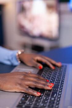 Close up of dark skinned business woman typing on laptop computer late in the evening from home office. Employee using modern technology network wireless doing overtime. photo