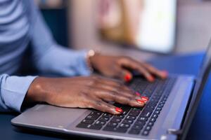 Close up of busy african woman typing on keyboard while she sits at home office. Employee using modern technology network wireless doing overtime. photo