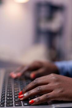 African american in living room using laptop computer sitting at desk at night . Employee using modern technology network wireless doing overtime. photo
