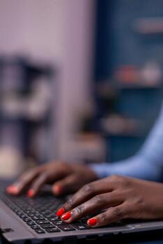 African american in living room using laptop computer sitting at desk at night. Employee using modern technology network wireless doing overtime. photo