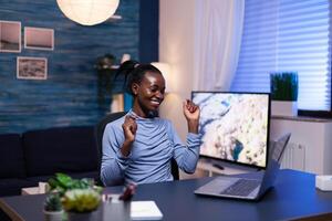 Cheerful darked skinned woman in the course of work from home in living room using laptop. Black woman enjoy e-learning process, easy application usage overtime. photo