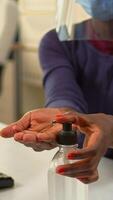Close up of black woman using hand sanitizer while working in office room in new normal company workplace. African employee cleaning disinfecting hands using alcohol gel against corona virus. photo
