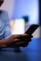 Close up of dark skinned woman chatting using smartphone in the evening from home office working remote. Employee using modern technology network wireless doing overtime. photo