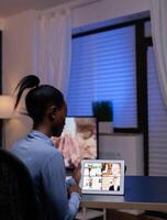 Dark skinned freelancer having werbcam conference on tablet pc from home office late at night. Lady using notebook with network wireless talking on virtual meeting . photo