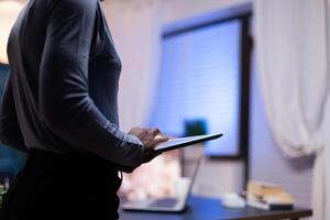 Close up of dark skinned woman working on tablet pc trying to finish a deadline. Busy focused employee using modern technology network wireless doing overtime writing. photo