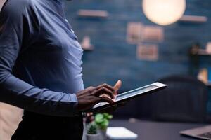 African business woman typing on tablet pc in the course of late night hours. Busy focused employee using modern technology network wireless doing overtime writing. photo