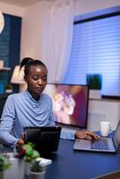 African freelancer using tablet pc working from home working late at night. Busy focused employee using modern technology network wireless doing overtime writing. photo