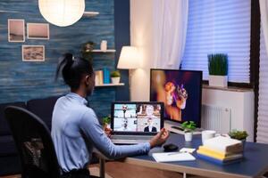 Dark skinned entrepreneur consulting with colleagues remotely from home late in the evening. Using modern technology network wireless talking on virtual meeting doing overtime. photo