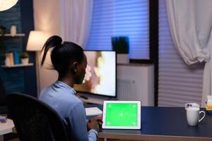 African freelance woman enjoying working from home looking at tablet pc with copy space availablesitting at desk. Using mockup chroma key display computer. photo