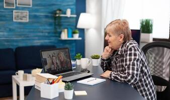 Cheerful senior woman talking with granddaughter during conference. Happy grandmother communicating with family via online web internet conference using modern internet technology while sitting in the living room photo