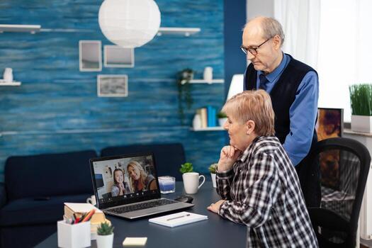 Senior man and woman talking with niece on call. Happy grandparents communicating with family via online web internet conference using modern internet technology while sitting in the living room photo