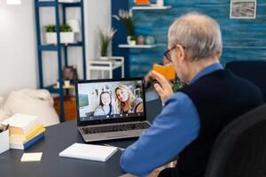 antiguo padre saludar hija durante conferencia en portátil computadora. contento abuelo diciendo Hola en el curso de en línea conferencia con familia desde vivo habitación. foto