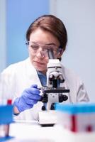 Caucasian woman scientist in white coat looking in high end microscope for pharmacy expertise. Modern laboratory for scientific research with professional equipment for studying virus and vaccine science development photo