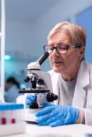 Senior scientist chemist analysing reaction of virus on microscope in laboratory. Woman working on science vaccine chemistry experiment in modern lab, analyzing pharmaceutical work for healtcare photo