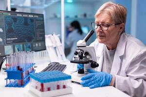Pharmacy senior scientist working with professional microscope in clinic discovery. Modern lab with research equipment for virus study and vaccine science development photo