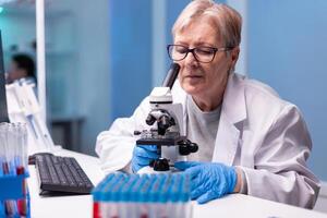 Senior doctor in white coat looking into microscope in laboratory discovery. Modern lab with research equipment for virus study and vaccine science development photo