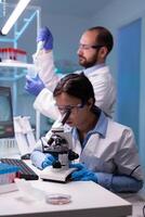 Chemist researchers working in laboratory with micropipette and microscope. Modern lab for scientific research with professional equipment for vaccine development diagnosing virus evolution. photo