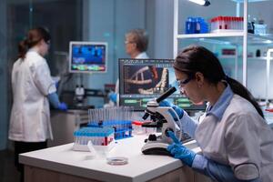 Biochemist scientists studying reaction of virus on microscope in laboratory. Research chemists working in lab with high tech analyzing blood and genetic material samples with special program photo
